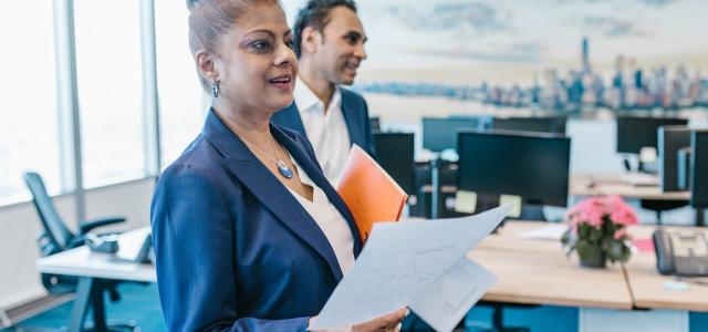 Woman in a suit holding a piece of paper. She is in an office setting.